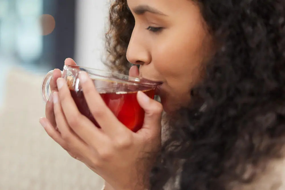 Mulher de lado segurando xícara transparente e tomando bebida diurética vermelha
