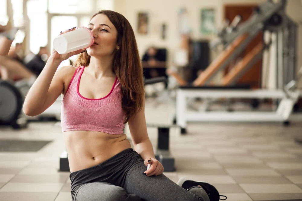 Mulher usando roupas esportivas sentada tomando suplemento