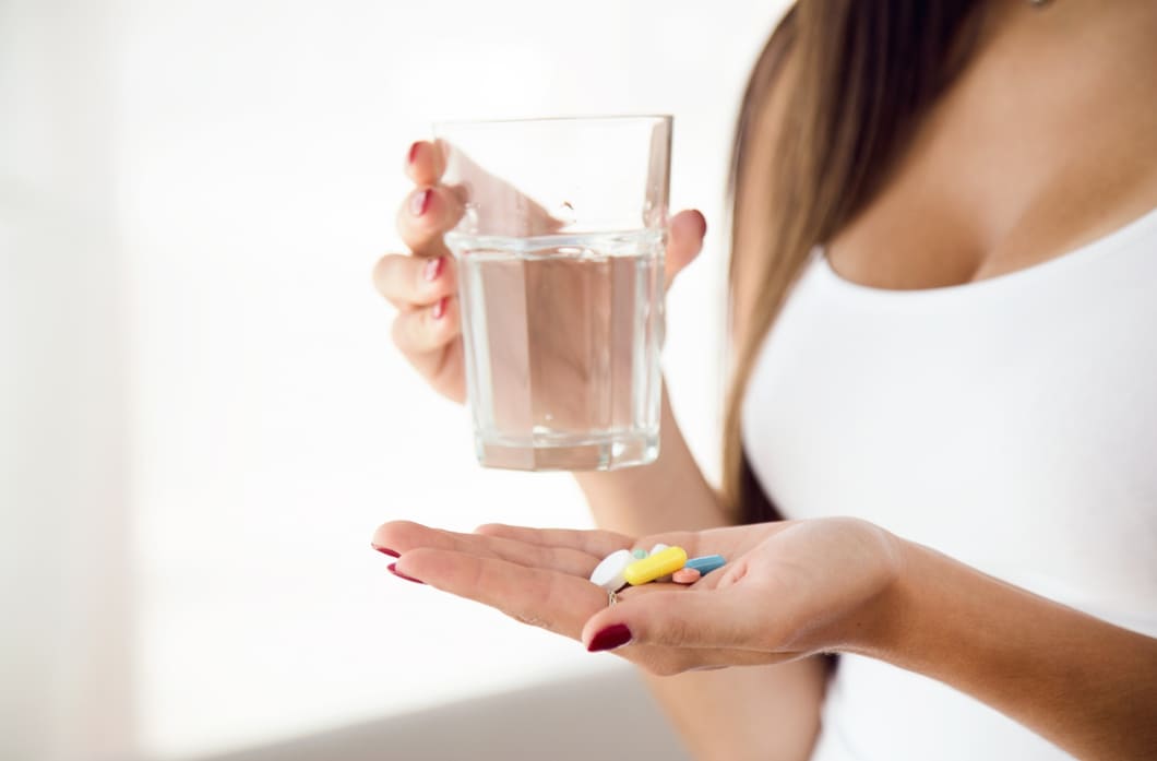 mulher-tomando-suplementos-e-vitaminas-sobre-um-fundo-branco