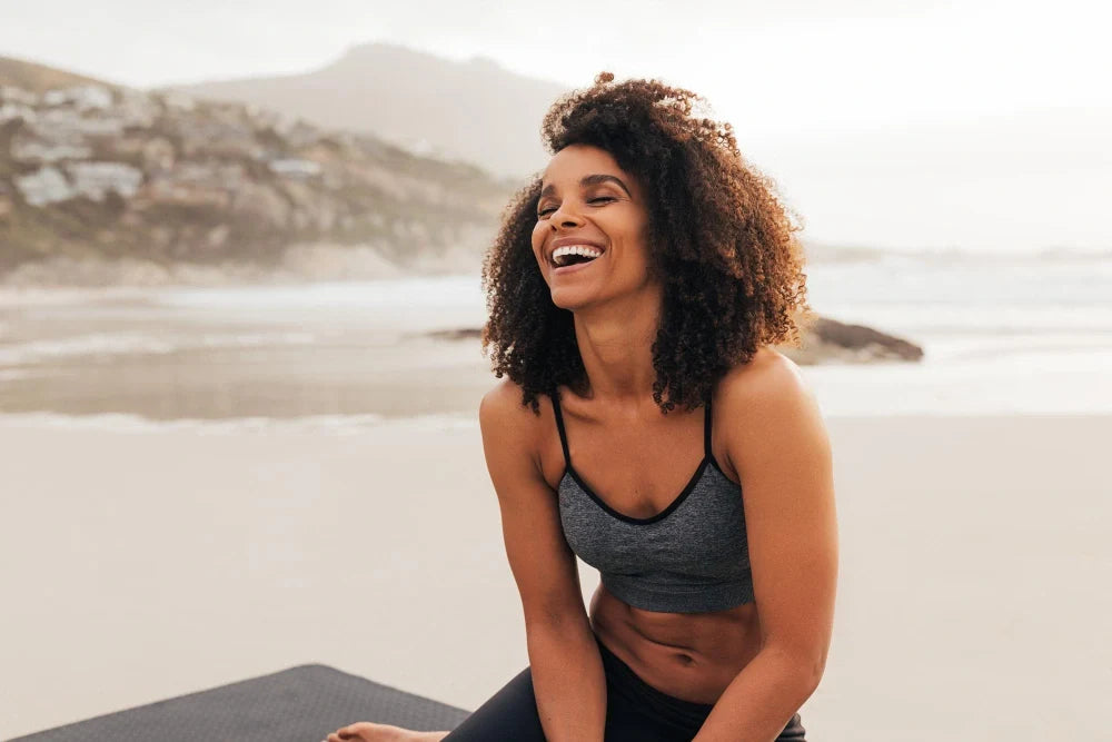 Mulher em praia sorrindo praticando Wellness