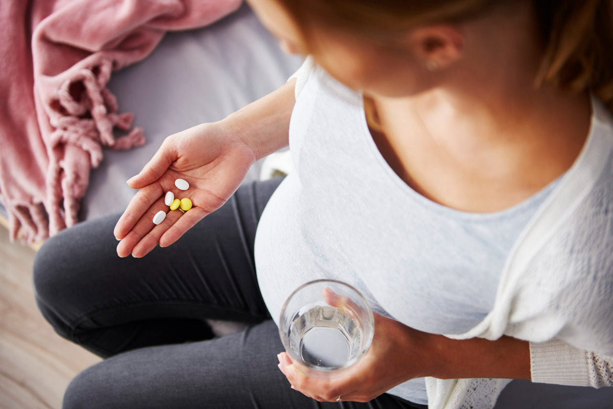 mulher segurando um copo com agua com uma mao enquanto a outra mao segura comprimidos de vitaminas e suplementos desin
