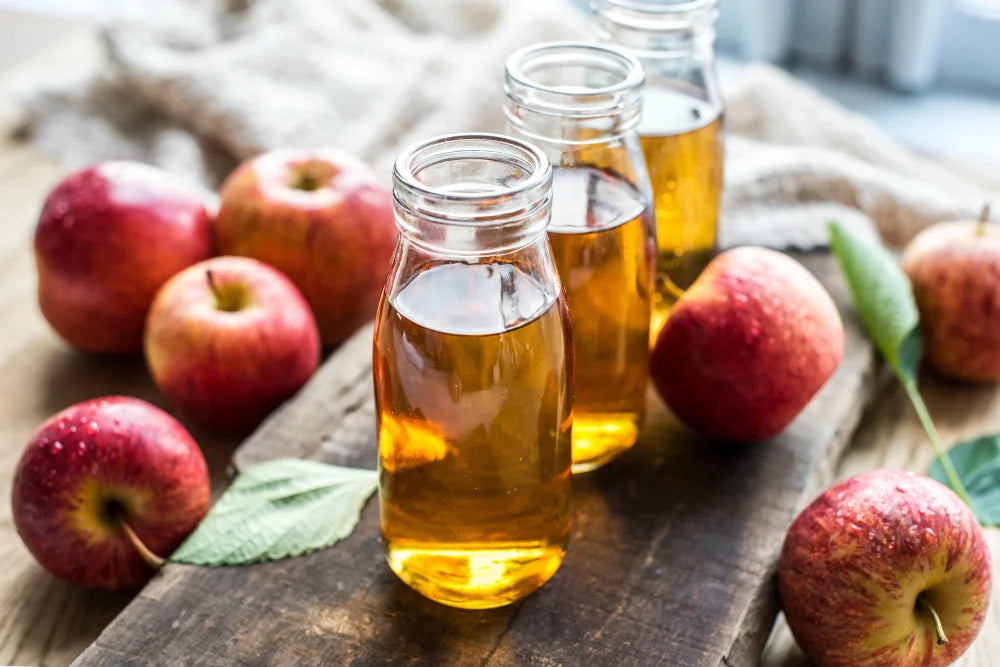 Garrafas de vinagre de maça ao lado da fruta maça em tábua de madeira