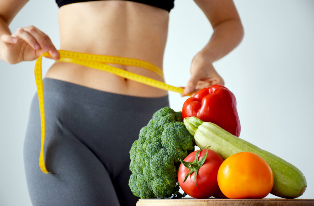 Desinchá mulher utilizando uma fita metrica na cintura perto de vegetais para começar uma dieta (2)
