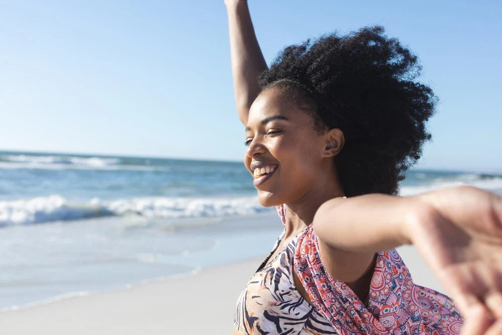 Mulher sorrindo em praia com os braços abertos tomando cuidados com a saúde no verão