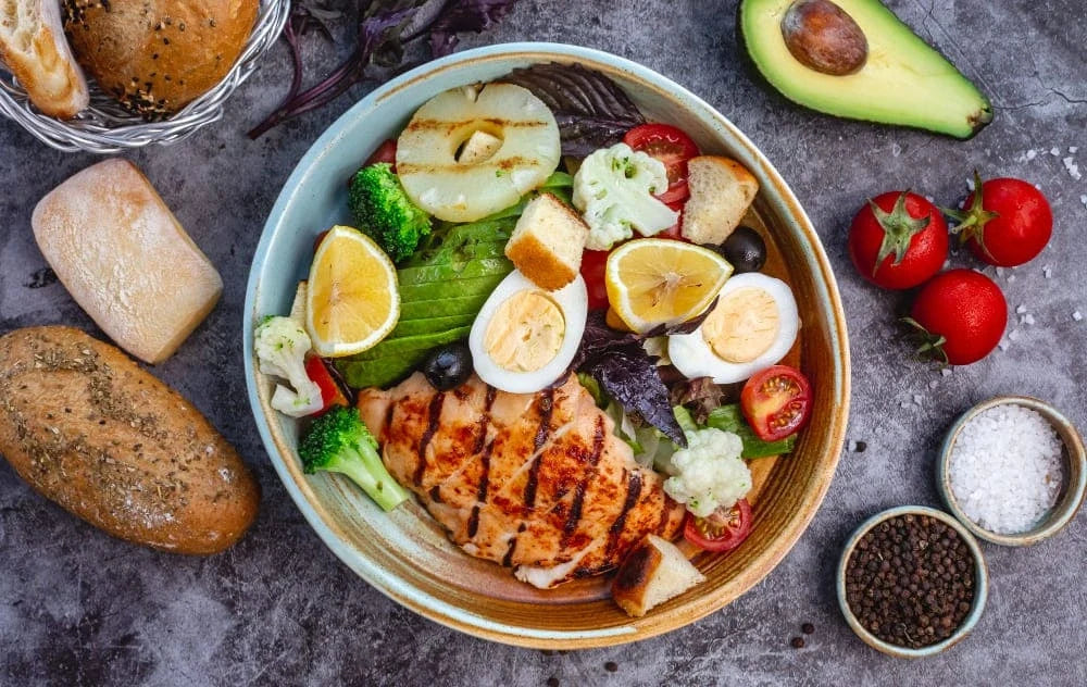 Vista superior de salada com brócolis, ovos, frango grelhado, tomate e folhas.
