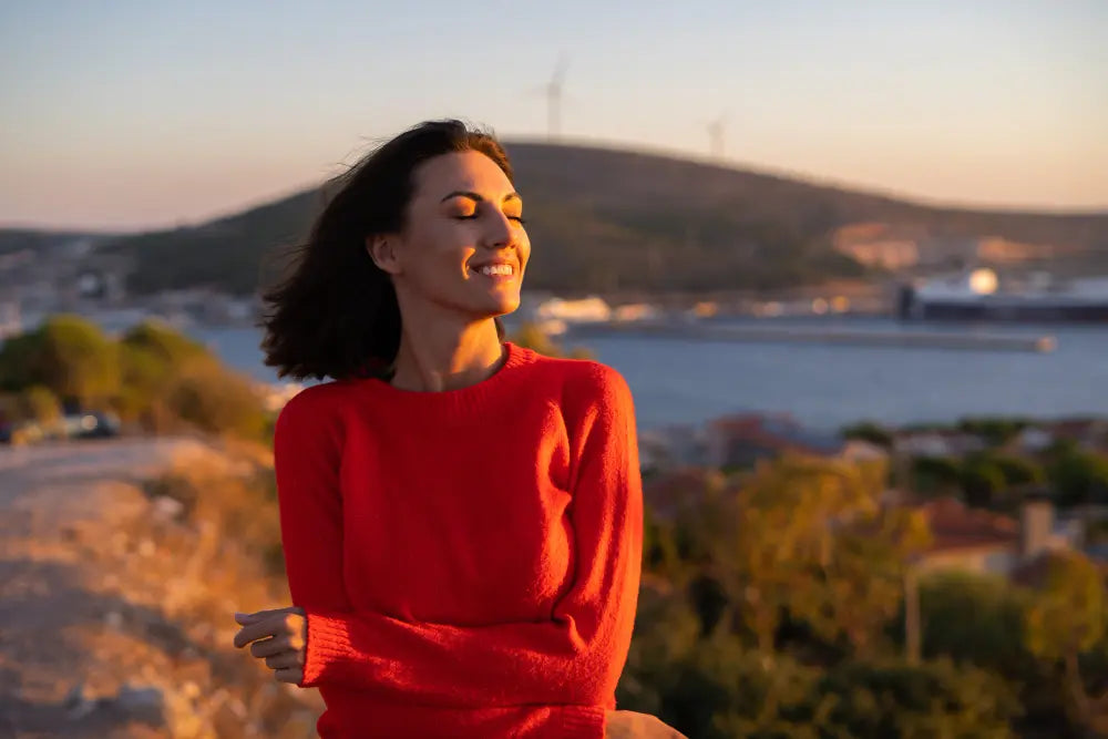 Mulher de olhos fechados sorrindo ao abraçar a si mesma em fundo desfocado de paisagem