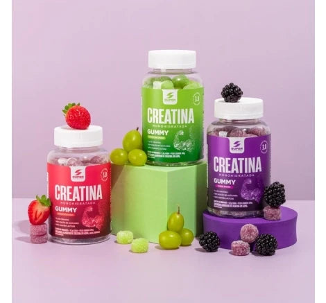 Três frascos de creatina gummy da Desinchá com frutas dos respectivos sabores ao redor: morango, uva verde e amora.