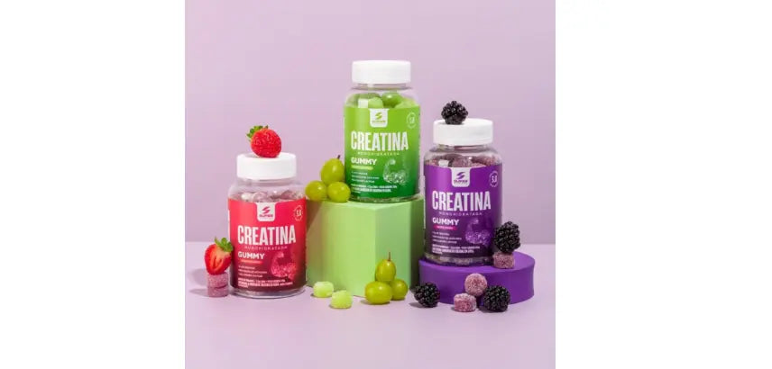 Três frascos de creatina gummy da Desinchá com frutas dos respectivos sabores ao redor: morango, uva verde e amora.