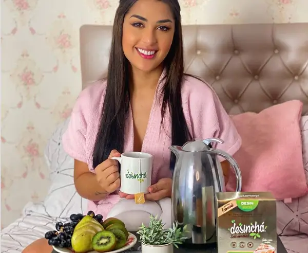 Mulher segurando uma xícara de chá da Desinchá, tomando café da manhã na cama