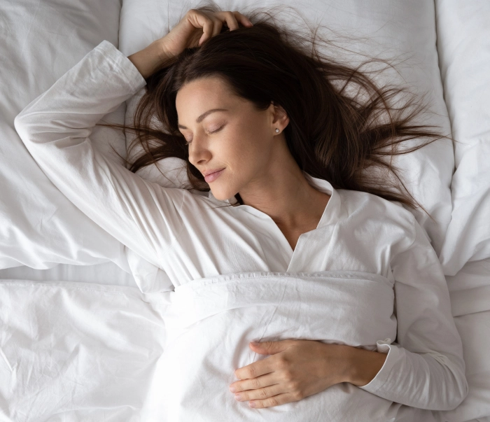 Mulher de pijama branco dormindo embaixo de um cobertor