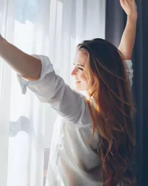 Mulher em frente a uma janela sorrindo para o sol