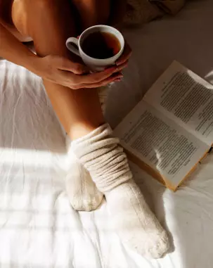 Mulher lendo um livro enquanto bebe uma xícara de chá Desinchá