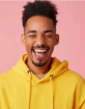 Homem de moletom amarelo com sorriso largo no rosto e fundo rosa