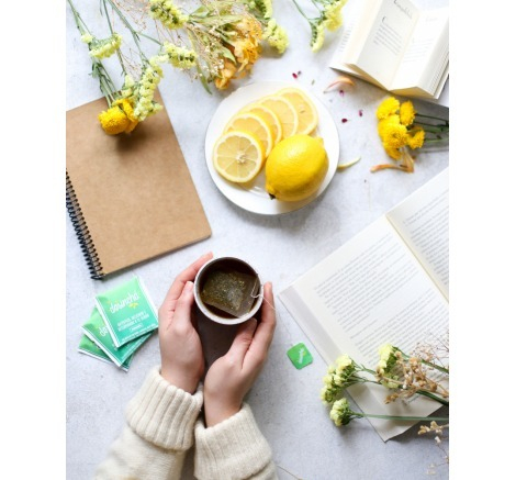 Mulher tomando Desinchá Sabores Abacaxi com Limão Siciliano ao lado de um prato de limões fatiados