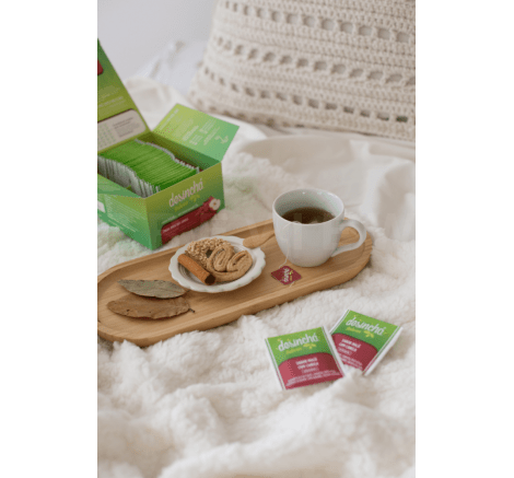 Xícara de chá de maçã com canela em uma bandeja, ao lado da embalagem do produto