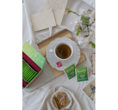 Xícara de Desinchá Pitaya com Blueberry em cima da cama, acompanhada da embalagem e sachês do produto